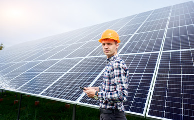 Male engineer in helmet with tablet in hands standing near solar panels. Concept ecology protection.