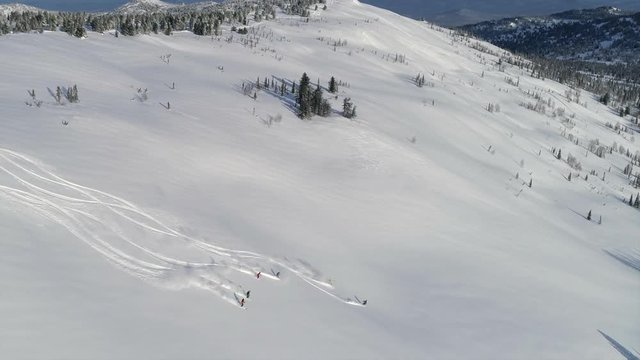 Aerial: Heli ski first track. Group of people skiing down the mountain valley. Epic free ride scene. Fresh powder. Skiing down the mountain with friends. Extreme freeride skiers skiing from the top