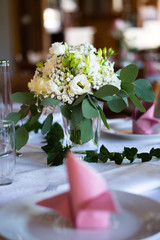 A bouquet constisting of white roses standing on a white table with a out of focus pink napkin in the foreground