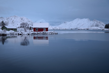 Typical red norwegian house by the sea with a beautiful view to the mountains. Located in small town Ballstad in Lofoten Islands. 