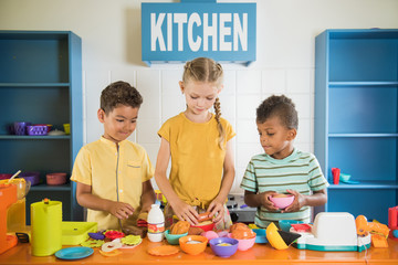 Happy kids playing with plastic tableware. Toy kitchen at playroom. Concept of happy childhood.