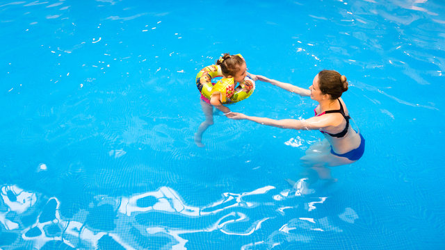 Kid and mother in aqua park. Little girl floating in pool with inflatable ring. Child at swimming lesson with mom.
