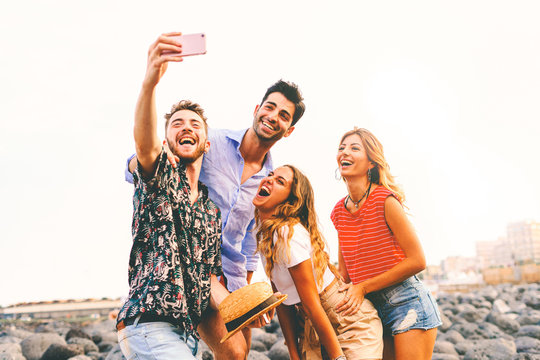 Group of young people having fun taking selfies with their smartphone outdoors in the summer. Friendship and vacation concept of youth using the new technologies in everyday life.