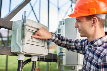 Close up of hand man engineer pushing button at the electrical equipment on solar power station with labeling: enable, disable. Ecology power conservation concept