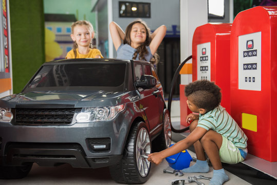 Kids At Gas Station In Playroom. Little Girl Sitting In Toy Car At Gas Station And Holding Dollars While Playing In Entertainment Center. Kids Role Game.