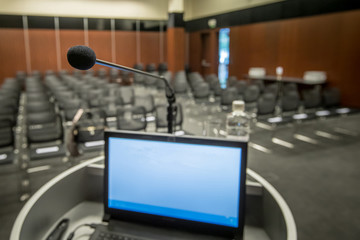 Speaker stage with microphone and a computer screen with a presentation and a bottle of water ready. Empty congress hall in the background.