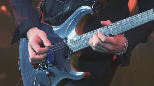 A virtuoso guitarist playing an electric guitar on stage with flashing LED lights.