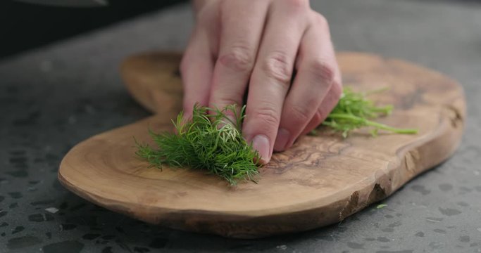 Slow motion man chopping dill on olive board
