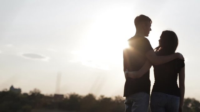A silhouette of a couple in love enjoys a beautiful sunset. A young and romantic couple is enjoying each other on a romantic summer evening. Happy couple talking and hugging at sunset