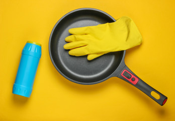 Washing dishes concept. Frying pan, gloves, detergent bottle on a yellow background. Top view