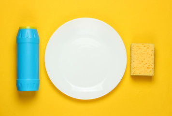 Washing dishes concept. Plate with a sponge, bottle of detergent on yellow background. Top view