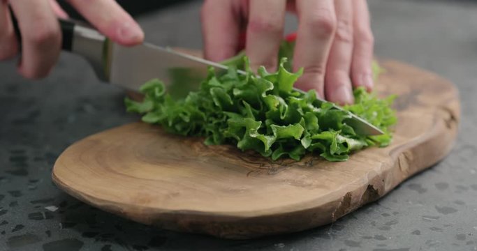 Slow motion man chopping frisee salad leaves on olive board