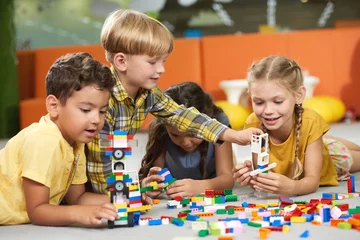 Fotobehang Lego 31.07.2017 - Kyiv, Ukraine. Kids playing with constructor toys. Cheerful kid girl building block toys while laying on the floor. Happy childhood concept.  © DenisProduction.com