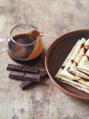 Pancakes poured with chocolate icing to the Shrovetide on a wooden brown background with a glass vase with chocolate icing. Place for text. Brown wooden background.