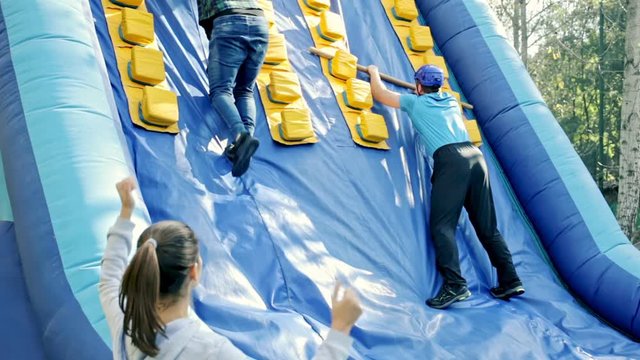 Group of excited people passing obstacles on inflatable arena at amusement park 