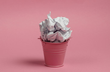 Mini bucket with crumpled piece of paper on a pink background.