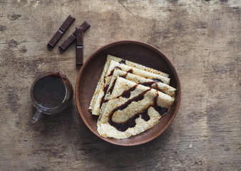 Pancakes poured with chocolate icing to the Shrovetide on a wooden brown background with a glass vase with chocolate icing. Place for text. Brown wooden background.