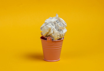 Mini bucket with crumpled piece of paper on yellow background.