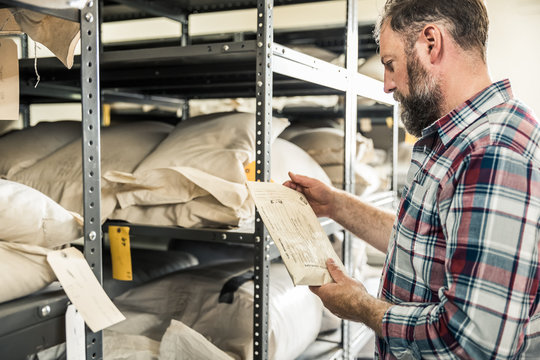 Farmer going through stock of seed collection in storage with laptop. Montana, USA
