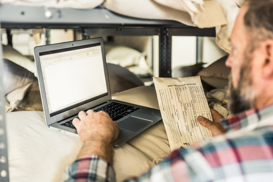 Farmer going through stock of seed collection in storage with laptop. Montana, USA