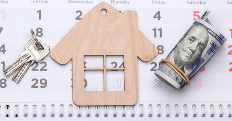 Payment of rent for housing. Mini house figurine, dollar bills on calendar.