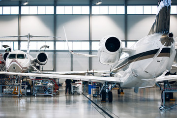 Airplane in a white hangar for maintenance. Inspection and repair works of private jet - obrazy, fototapety, plakaty