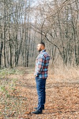 Bearded hipster man with serious face is thinking about something while standing outdoors against autumn fall with copy space, stylish brutal male with trendy look walking in park at sunset.