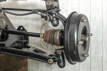 Front suspension members of an older car with new brake drum exposed with spindle, ball joints and steering rack visible.