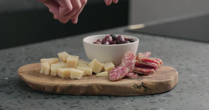 Slow motion man hand takes olives, cheese and fuet from olive wood board