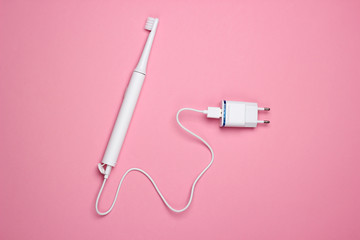 Modern electric toothbrush with a charger on a pink pastel background. Top view