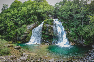 Fototapeta na wymiar Aerial panorama of magical looking Virje waterfall in Slovenia, close to bovec. Dreamy and enchanting water falling down the cliff above the small alpine lake.