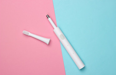 Modern electric toothbrush with nozzle on pink blue background. Top view