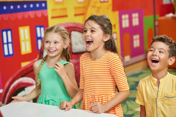Three excited kids in playroom. Happy smiling children indoor. Kids entertainment in kids club.