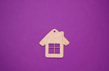 Wooden house figurine or keychain on purple background. Top view