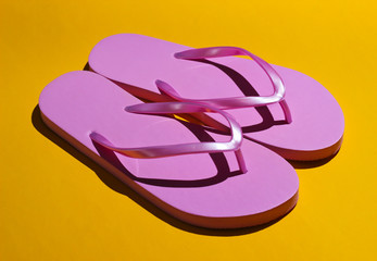 Pink flip flops on a yellow background. Fashion studio shot with shadows.