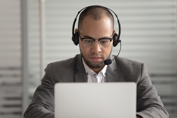 Focused male employee in headset busy working on laptop