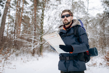 Handsome bearded hiker checking a map to orientate in snow-clad forest