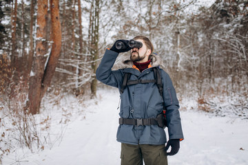 Fototapeta na wymiar Tourist ranger in fur hood anorak looking into the distance using binoculars