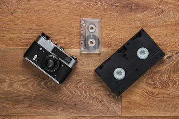 Video cassettes, audio cassette, old-fashioned film camera on the floor. Retro media 80s. Top view