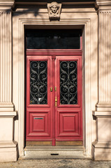 Classical European doorway with stone pillars around red door with gold details,. Ornate details in dark windows and stone figurine over entrance. Shot in bright daylight