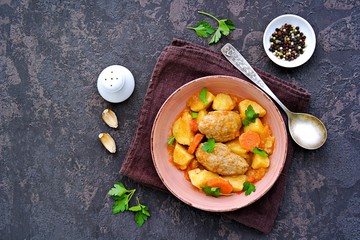 Hearty stew with potatoes, carrots and chicken meatballs in a pink bowl on a dark concrete background. Copyspace. Top view.