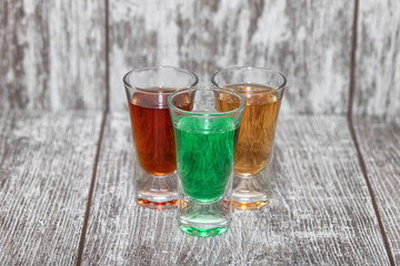 Three shots with different alcoholic beverages stand on a wooden stand