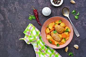 Hearty stew with potatoes, carrots and chicken meat balls in a pink bowl on a dark concrete background. Copyspace. Top view.