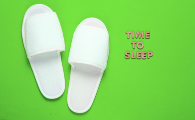 Time to sleep. White sleeping hotel slippers on a green background
