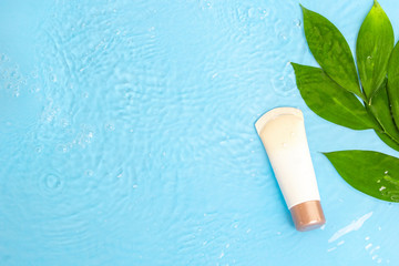 Sunscreen cream spf lotion to remedy skin from sun with green leaves on blue water surface of pool, top view. Concept ultraviolet protection, summer cosmetics. Natural organic beauty product