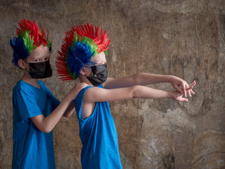 Two boys in black medical masks and carnival colored punk wigs are quarantined at home. Children cough badly. concept of fight against the coronavirus epidemic and proper prevention of infections