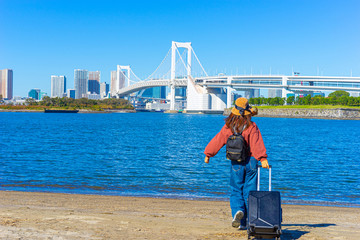 Odaiba island. Japan. Rainbow Bridge in Tokyo. Tourist near the Pacific Gulf. Girl with a suitcase near the rainbow bridge. Trip to the island of Odaiba. Trash island in Japan. Cruise to Japan.