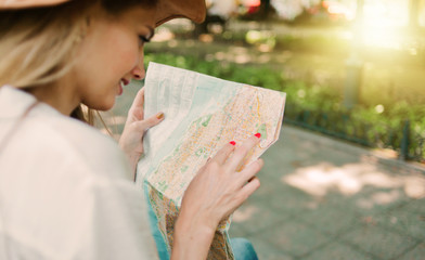 Blonde woman in a felt hat looks at city map in unfamiliar city outdoor
