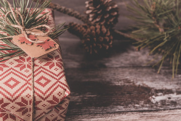 Closeup of Christmas present with rustic gift wrapped in retro wrapping paper with natural vintage twine as decor on old wood floor with spruce twig and pinecones in the background with copyspace