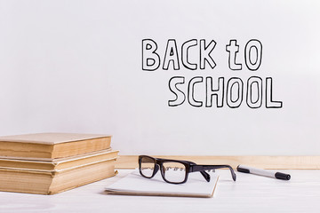 The inscription marker on a white board, Back to School. A table with books and glasses.